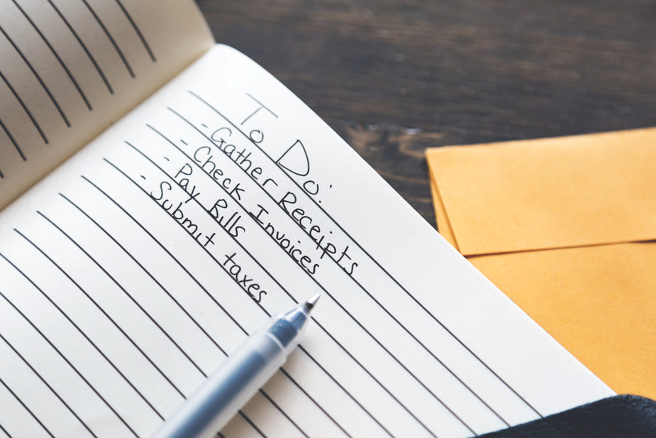 A tax time to do list is written out in pen in a notebook on a desk, with an envelope underneath.