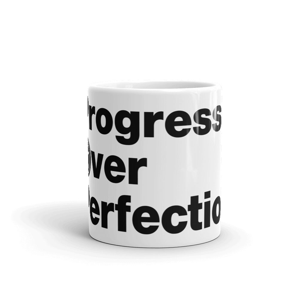 Black, Progress Over Perfection, words, stacked, left aligned. 'O' in Over is round universal icon, on front of white coffee mug, middle side view.